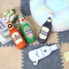 A collection of plush beer bottle dog toys in various colors and textures resting on a fuzzy surface.
