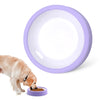 A dog is feeding from a purple slow feeder bowl, next to a large purple ceramic bowl.