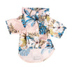 A pink dog shirt with a tropical leaf print featuring blue and yellow foliage.