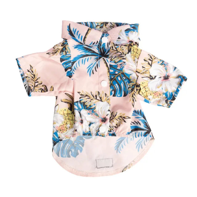 A pink dog shirt with a tropical leaf print featuring blue and yellow foliage.