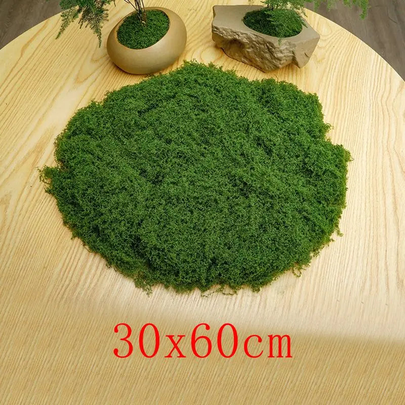 A patch of vibrant green preserved moss on a light wooden surface, with a small potted moss in the background.