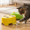A tabby cat is playing with a yellow interactive toy featuring a green base and yellow feathers on a wooden floor.