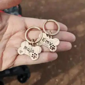 A hand holds a custom engraved bone-shaped stainless steel dog ID tag with the name Maya.