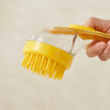 A hand holds a yellow silicone pet bathing brush with bristles dripping water.