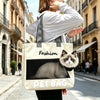 A person is carrying a beige pet bag with a black cat silhouette design on the front while walking outdoors.
