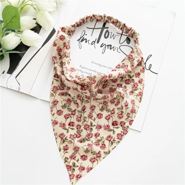 A floral patterned triangle scarf with pink and green leaves is displayed on white paper.
