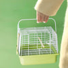 A hand is holding a white wire bird carrier bag with a green tray and perch against a light green background.