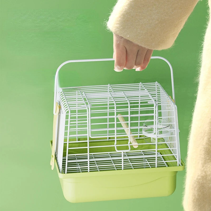 A hand is holding a white wire bird carrier bag with a green tray and perch against a light green background.