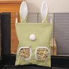 Un sac de foin à toile vert clair avec des formes d'oreilles blanches et de la litière de paille, montré dans un enclos sombr