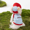 A fluffy white dog vest and hat with red and light blue fabric lying on green grass.