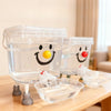 Distributeur d'eau automatique pour animaux en plastique transparent avec un visage souriant, sur une table en bois.