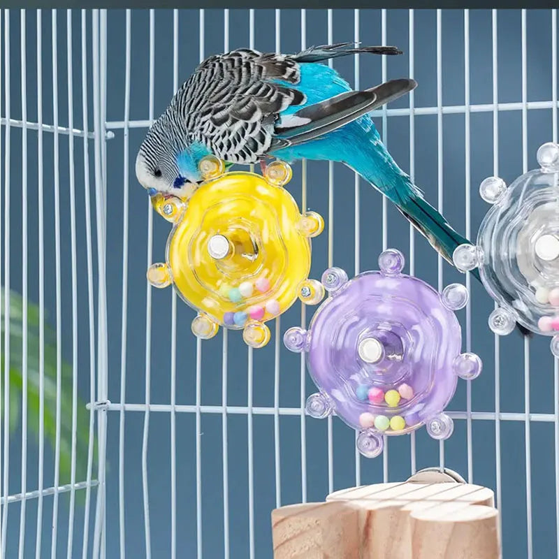 Ein blau-grauer Papagei-Spielzeug interagiert mit farbenfrohen rotierenden Leckerli-Dispensern in einem Drahtkäfig.