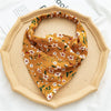 A mustard yellow bohemian paisley triangle head scarf folded on a light beige plate.