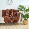 A brown microfiber blanket draped over a light-colored sofa next to a potted palm plant.