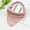 A pink bohemian paisley triangle scarf laid on a white surface next to a magazine.