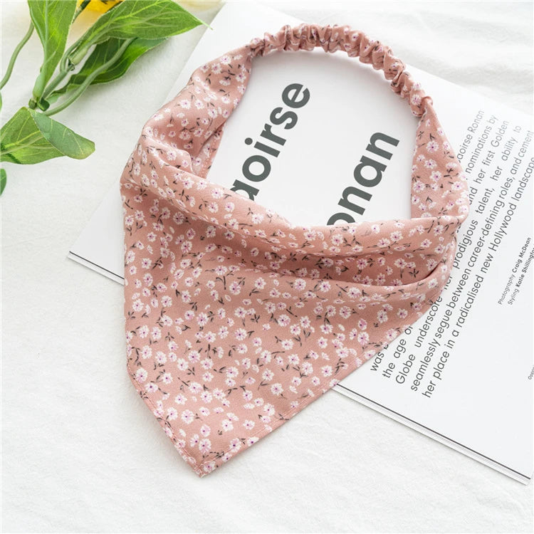 A pink bohemian paisley triangle scarf laid on a white surface next to a magazine.