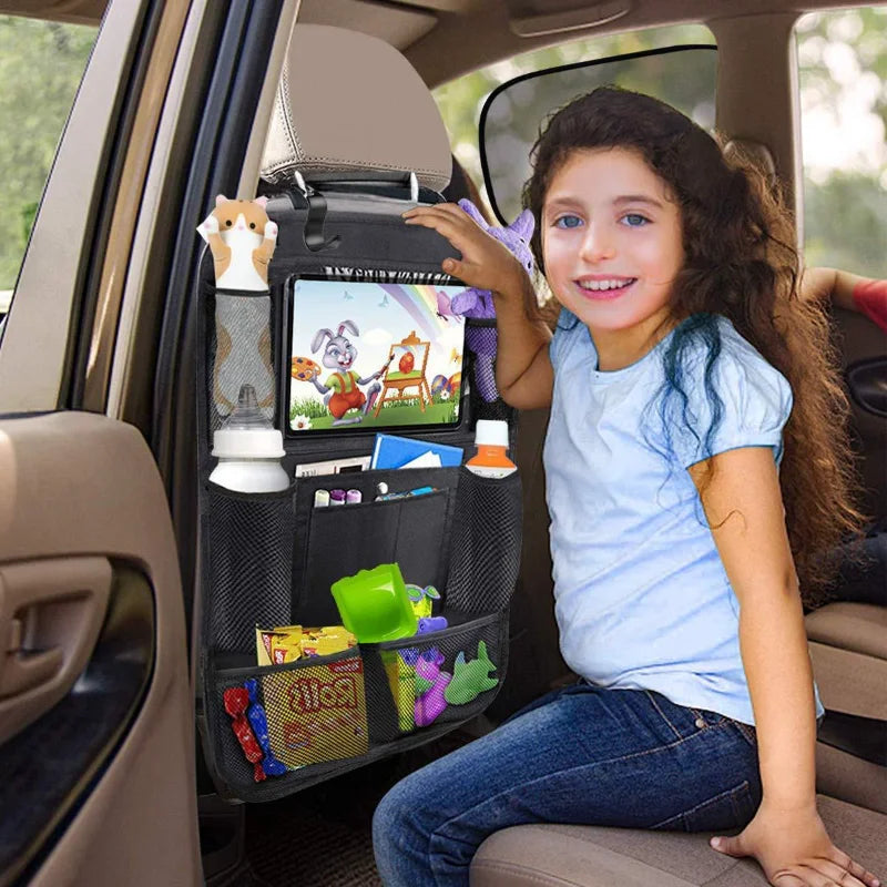 A smiling girl sits in a car backseat showing a black organizer with a tablet holder and storage pockets.