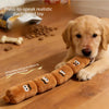 A golden dachshund puppy is lying down next to a line of soft, squeezable dog chew toys on a wooden floor.