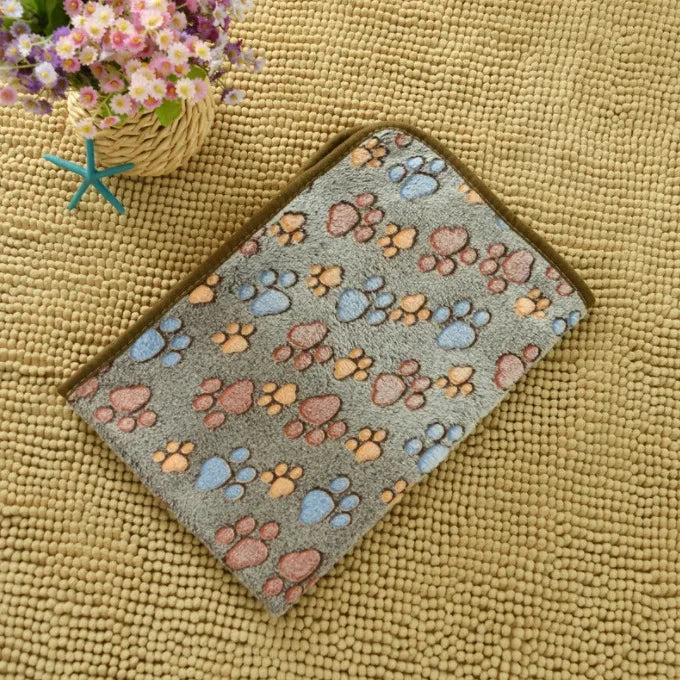 A gray pet bed mat cover featuring a pattern of paw prints in shades of pink, orange, and blue, resting on a yellow textured 