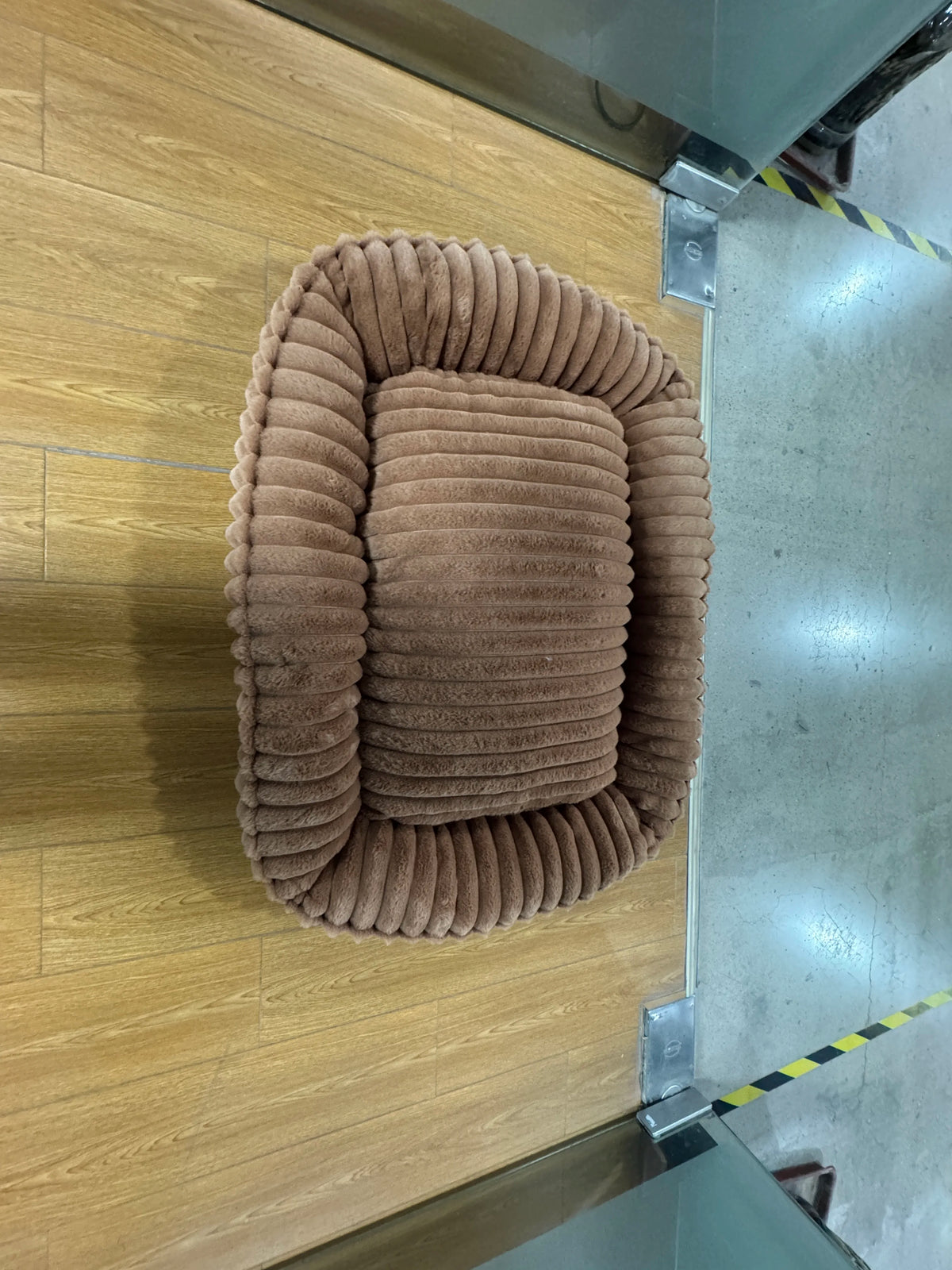 Un lit pour animaux rond et brun en peluche, conçu pour chiens et chats, monté sur une surface en bois clair.