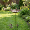 Station d'oiseaux en métal décorative avec un bol rond peu profond sur un support noir dans un jardin gazonné.