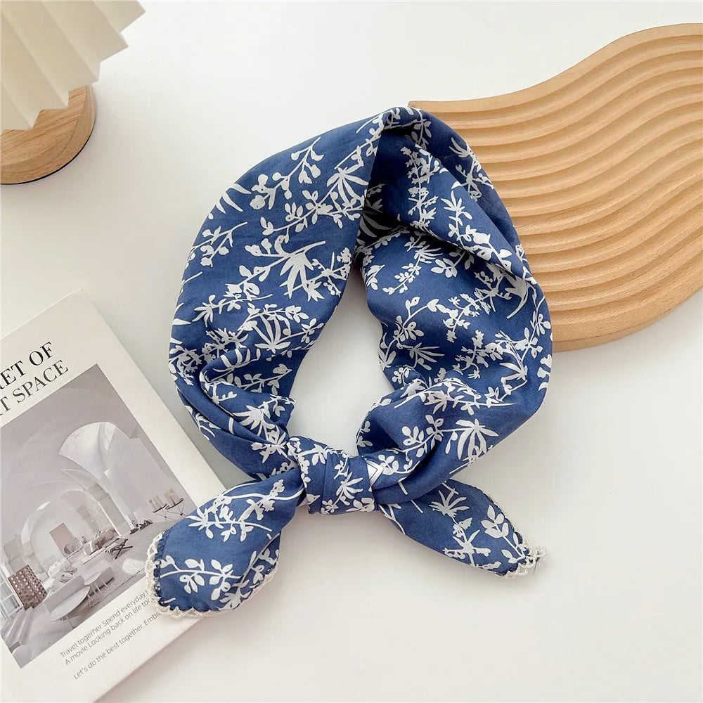 Foulard en coton bleu marine à motifs floraux noué en nœud, posé sur une surface claire à côté d'un objet en bois.