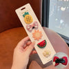 A hand holds a white card displaying five flower-shaped baby hair clips including a pineapple, bow, and watermelon slice.