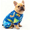 Un bouledogue français couleur faon portant une combinaison de flanelle hiver bleue avec des motifs jaunes et verts.
