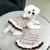 A fluffy white dog wearing a striped dress with pink bowknot and ruffle trim.