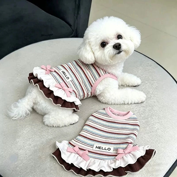 A fluffy white dog wearing a striped dress with pink bowknot and ruffle trim.