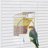 A green and yellow parrot is perched on a white automatic feeder designed for husk separation.
