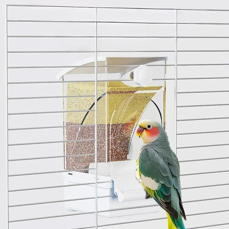 A green and yellow parrot is perched on a white automatic feeder designed for husk separation.