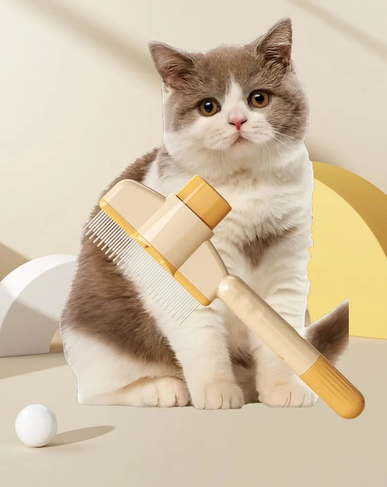 A fluffy gray and white kitten is sitting next to a yellow pet brush with massage pins.