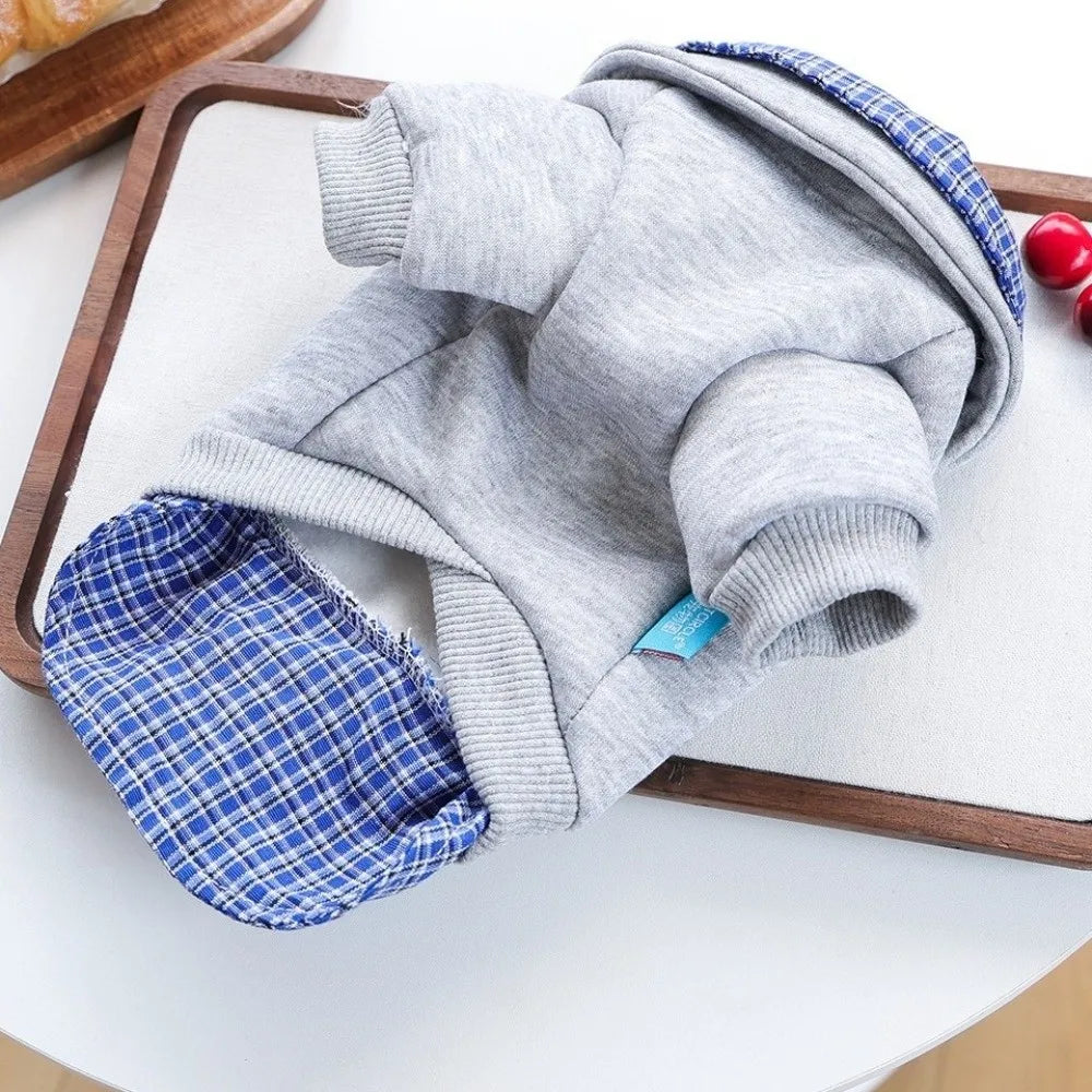 A gray and blue plaid dog hoodie is displayed on a wooden tray.