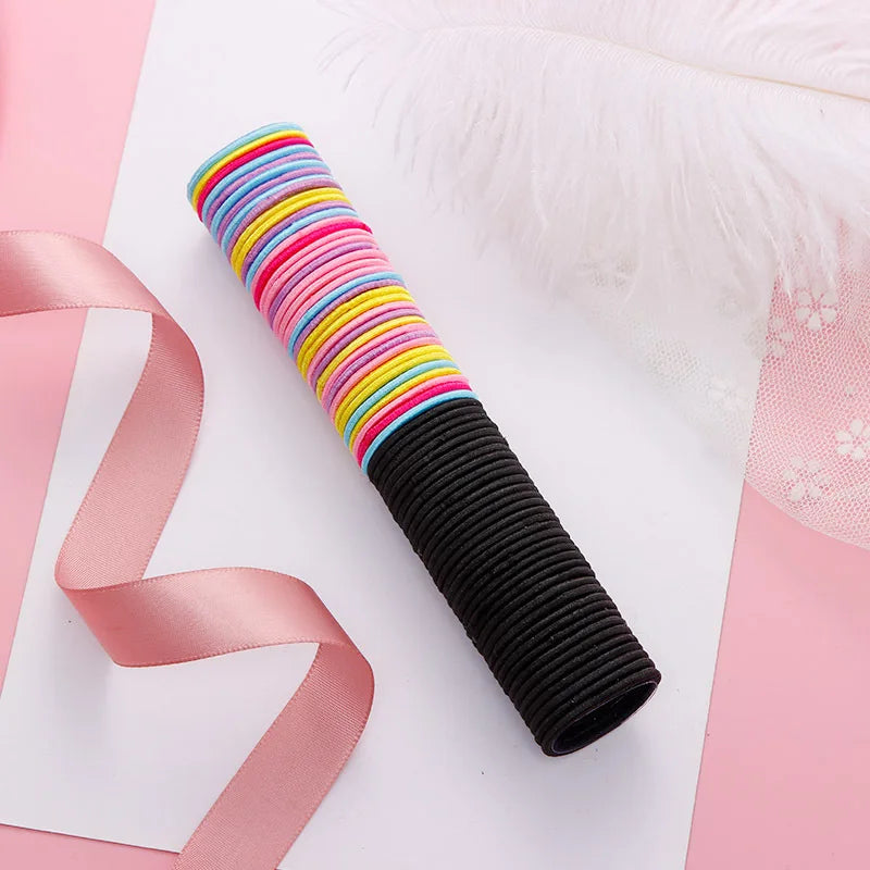 A stack of colorful elastic hair bands in various stripes and a black elastic band are displayed on white paper with pink acc