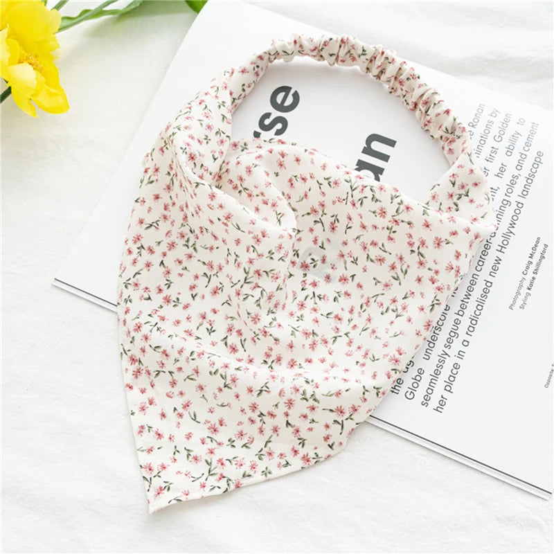 Diadema o pañuelo para el cabello con estampado floral rosa, exhibido sobre fondo blanco junto a una revista.