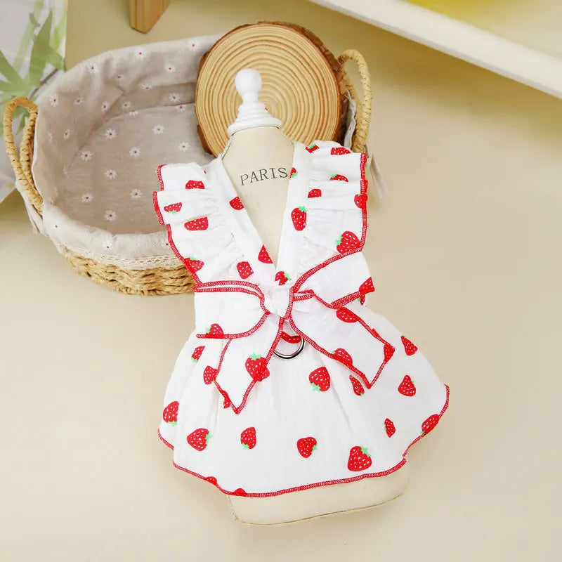 A white strawberry dog dress with red accents displayed on a mannequin next to a straw hat.