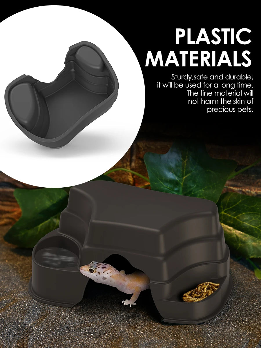 A dark gray plastic reptile hide cave decoration with food bowls, shown in use on a natural surface.