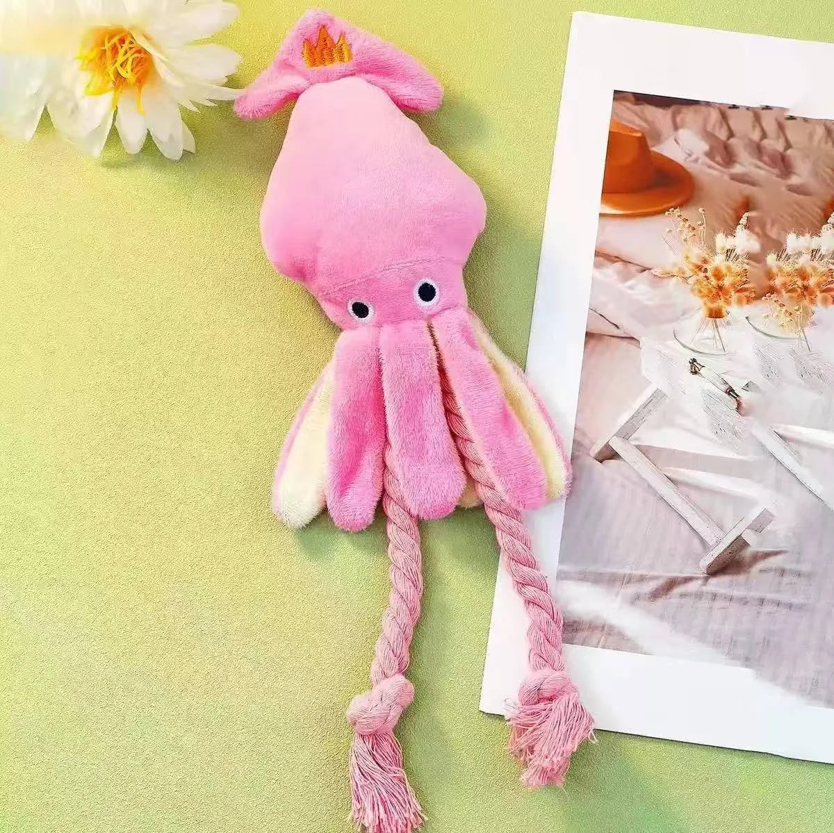 A pink squeaky octopus plush toy with yellow accents is displayed next to a framed photo.