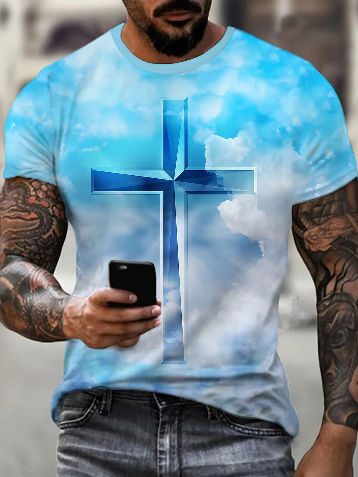A man wearing a light blue t-shirt featuring a large blue cross design against a cloudy sky.