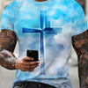 A man wearing a light blue t-shirt featuring a large blue cross design against a cloudy sky.