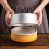 Hands hold a round aluminum cake pan set, showing the bottom and top pieces.
