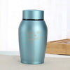 A light blue stainless steel pet memorial storage box with a black lid sitting on a white surface.