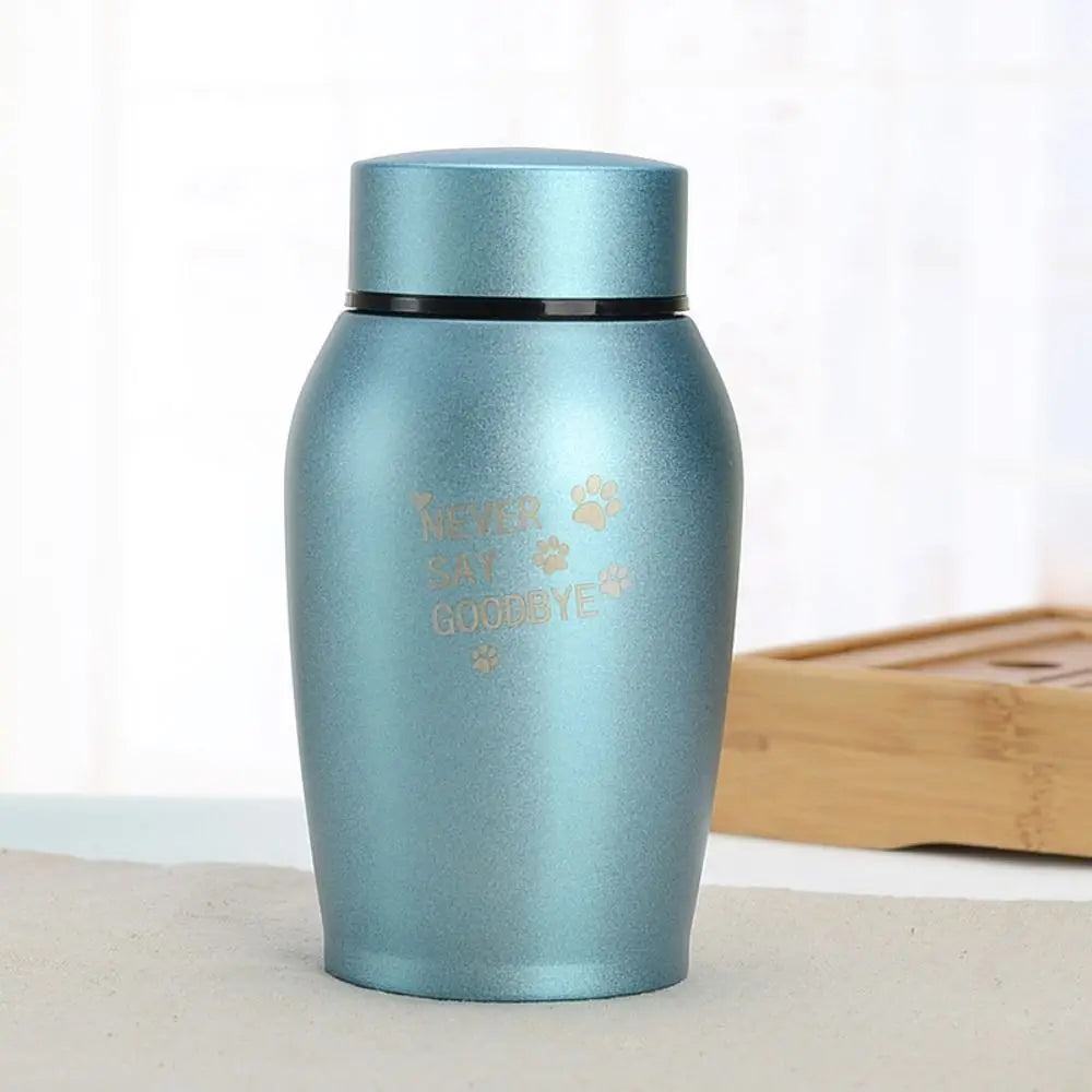 A light blue stainless steel pet memorial storage box with a black lid sitting on a white surface.