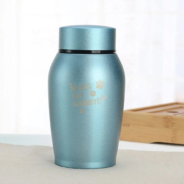 A light blue stainless steel pet memorial storage box with a black lid sitting on a white surface.