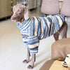 A light brown dog wearing a blue and yellow striped thermal fleece sweater standing on a floor.
