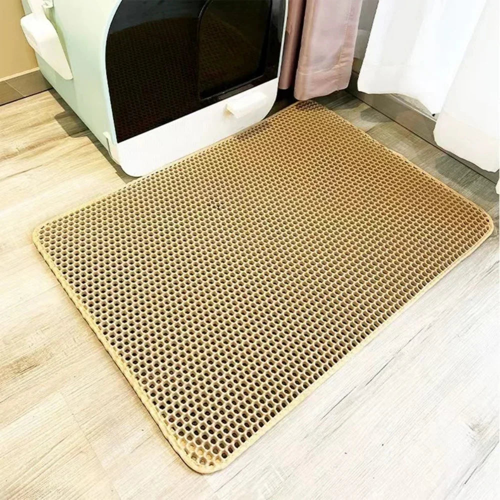 A beige, double-layer cat litter mat with a non-slip base placed on a light wooden floor.