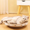 A white cat is relaxing on a round, bowl-shaped scratching pad indoors.