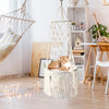 A fluffy orange cat is resting inside a large macrame hammock pet bed hanging in a bright, bohemian-style room.