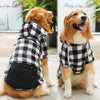 A golden retriever wearing a black and white plaid reversible jacket sits outdoors.